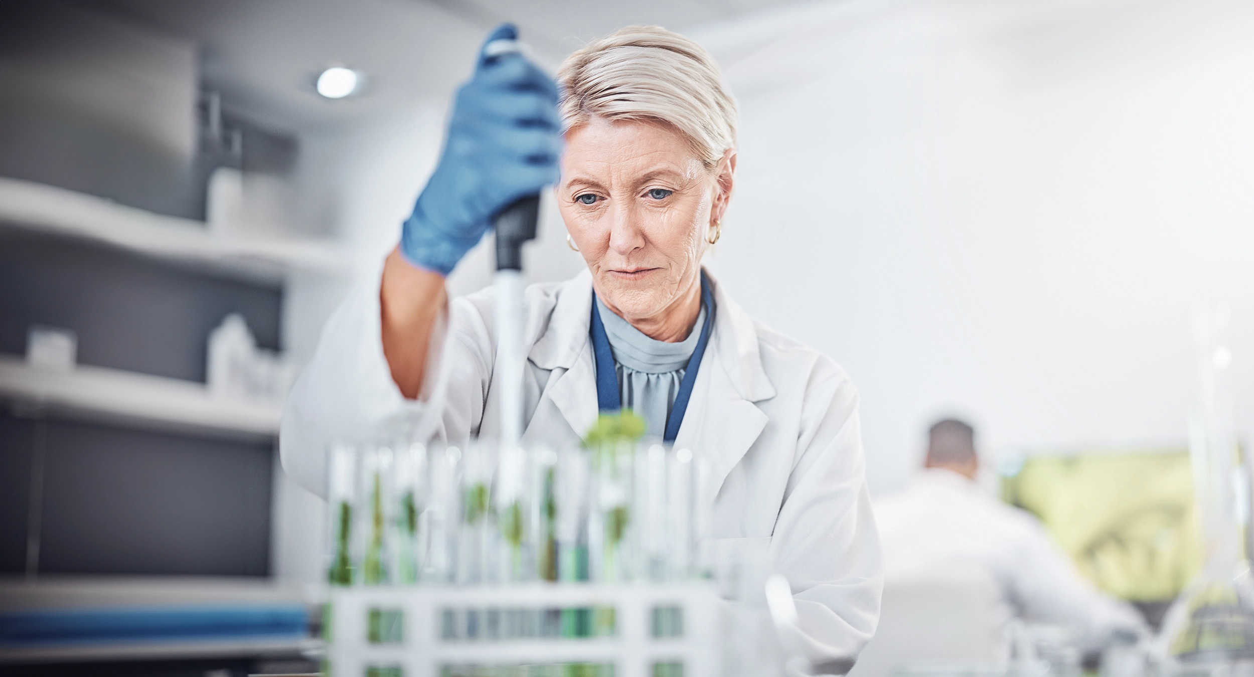 Woman wearing white lab coat using dropper tool to dispense liquid into test tubes Woman wearing white lab coat using dropper tool to dispense liquid into test tubes